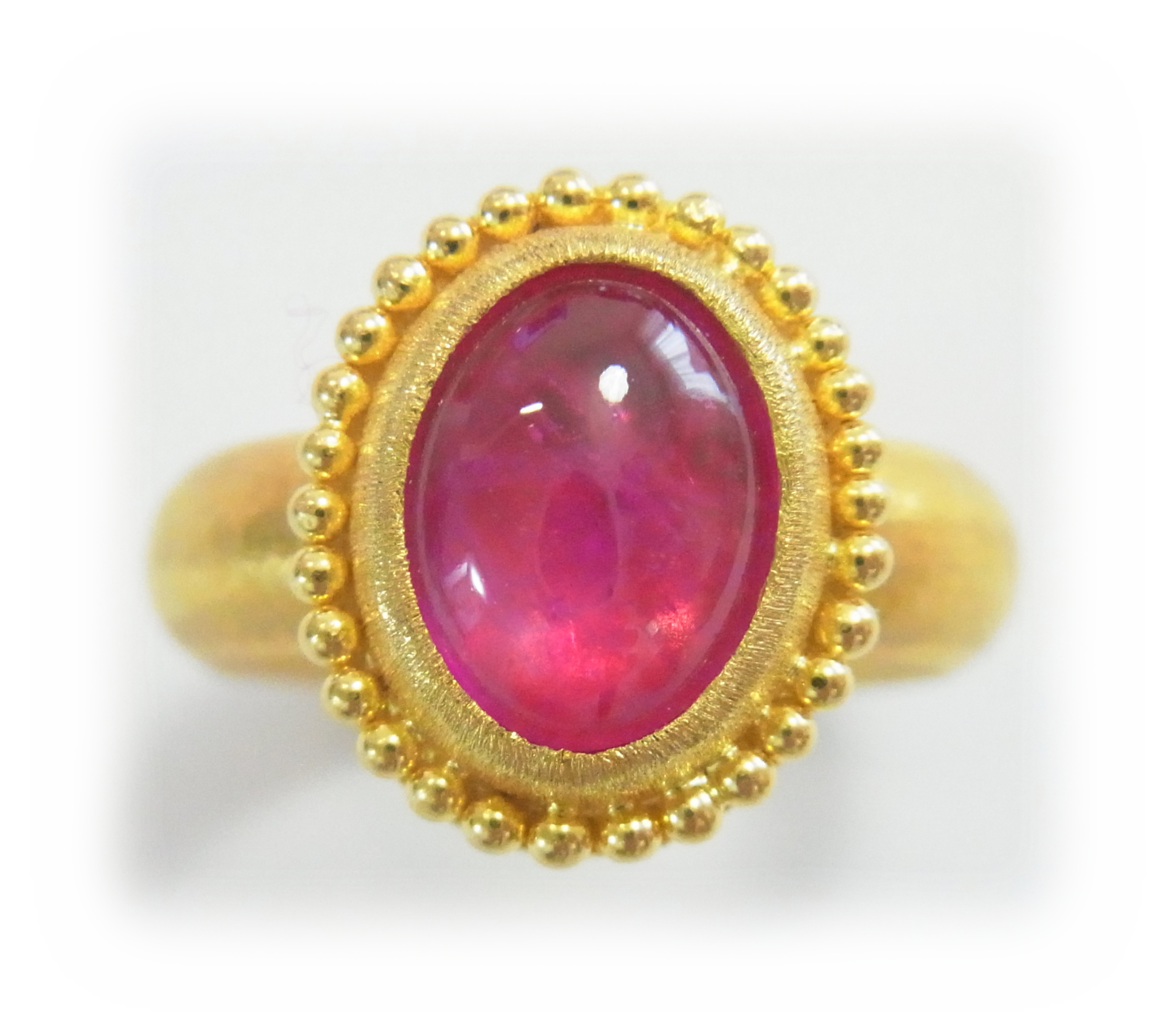 A gold ring with a cabochon-cut ruby viewd from directly above, with granulated gold trim around the bezel. 3