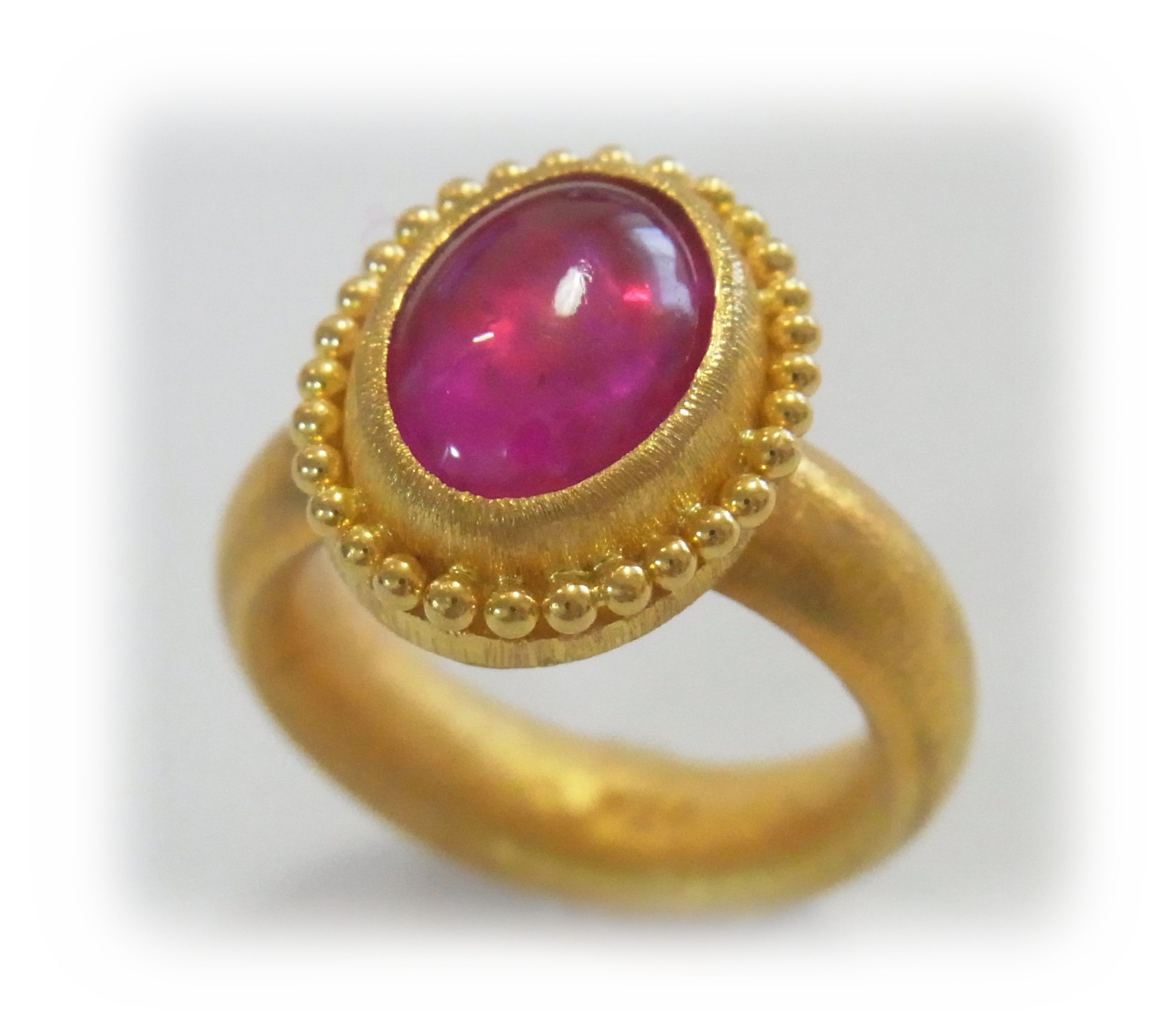 A gold ring with a cabochon-cut ruby, viewed from a diagonal angle above, with granulated gold trim around the bezel. 2