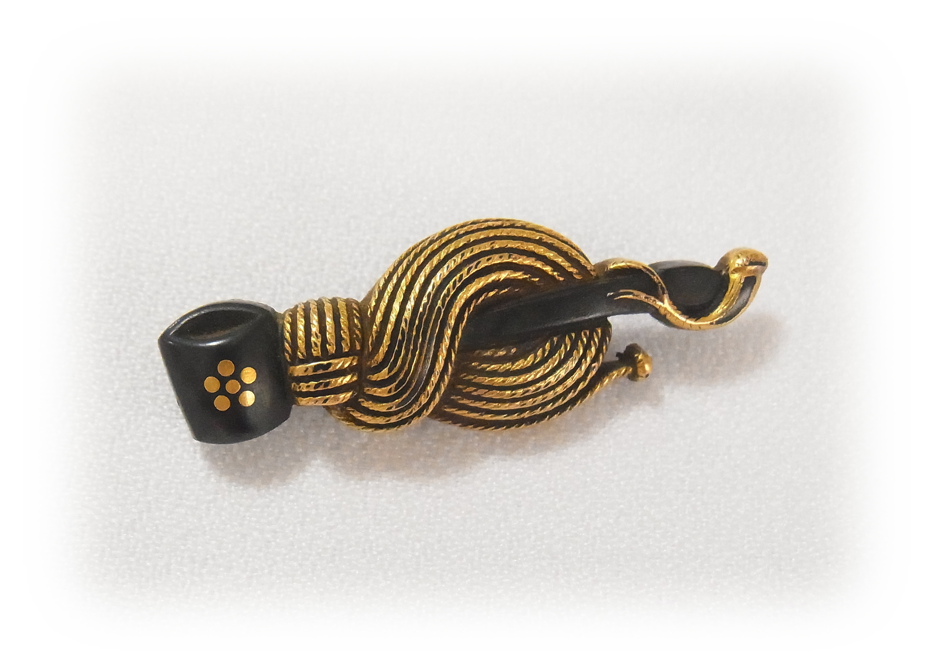It is a Metal fitting attached to portable pouch of tobacco leaves, and the name of the design is Ladle with gold family crest